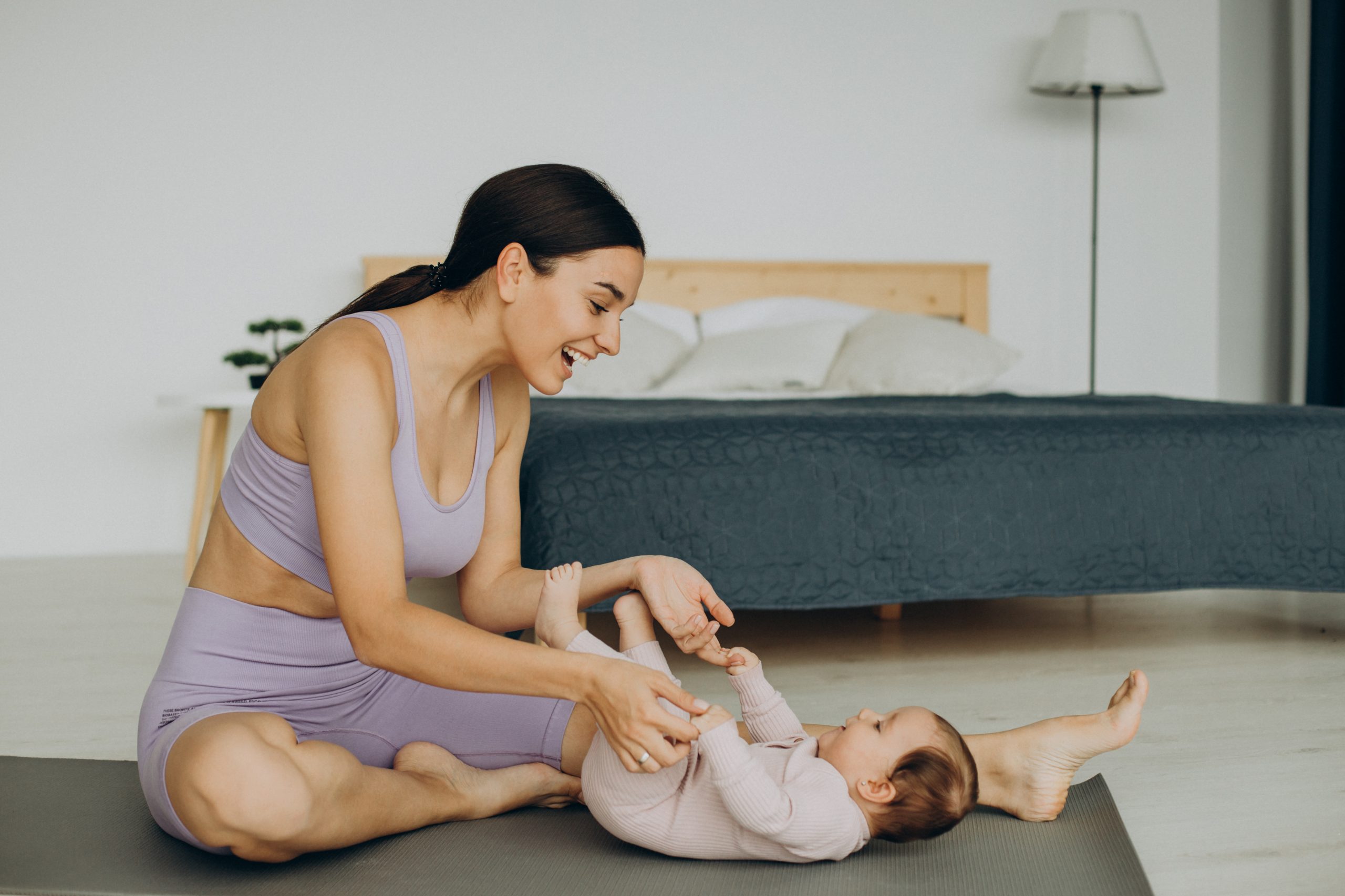 Mutter in Yogakleidung mir Baby spielend auf Yogamatte